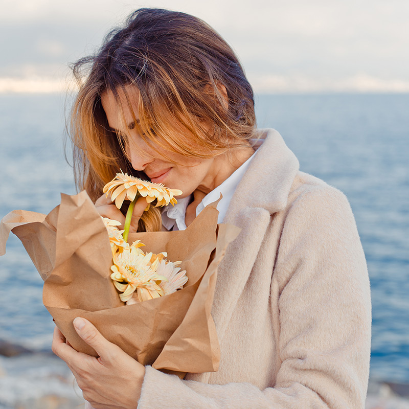 portrait-pretty-woman-standing-smelling-flowers-seaside-daytim