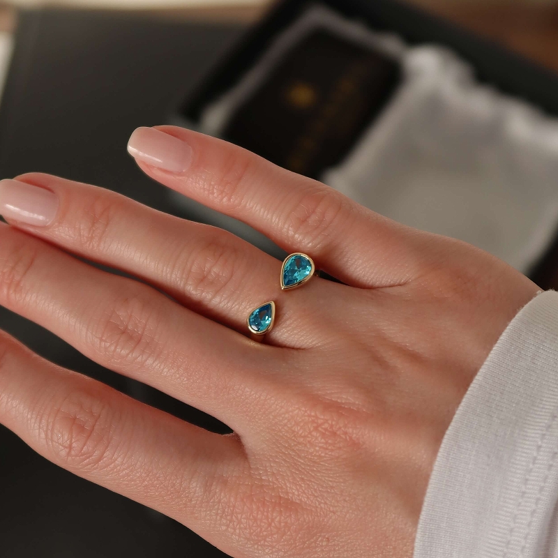 Close-up of gold teardrop blue gem open ring on hand